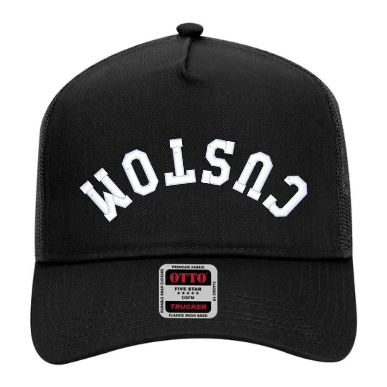 May include: Black trucker hat with a white "CUSTOM" logo embroidered on the front. The hat has a mesh back and a snap closure.