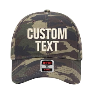 May include: A camouflage baseball cap with the words "CUSTOM TEXT" embroidered in white. The cap has a curved brim and a small tag with the brand name and fabric details. The cap is made of a durable fabric.