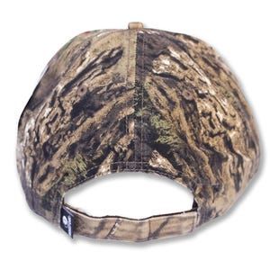 May include: A camouflage baseball cap with a curved brim. The cap features a brown, green, and tan pattern, with a small tag on the back. The cap is designed for outdoor activities and hunting.