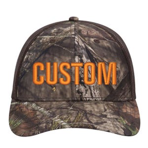 May include: A camouflage print baseball cap with a brown mesh back and a curved brim. The front panel features the word CUSTOM embroidered in bold, bright orange capital letters across the center of the woodland pattern fabric.