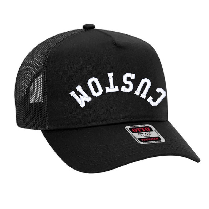May include: Black trucker hat with a white "CUSTOM" embroidered on the front in an arched design. The hat has a black mesh back and a red and white "OTTO" label.