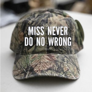 May include: A camouflage baseball cap with the text "MISS NEVER DO NO WRONG" in white block letters. The cap features a classic six-panel design with a curved brim, perfect for outdoor activities or casual wear.