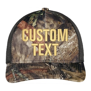 May include: A camouflage trucker hat with a black mesh back. The hat has gold embroidery that reads "CUSTOM TEXT".