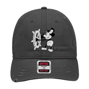 Puede incluir: Una gorra de papá negra desgastada con una imagen en blanco y negro de Mickey Mouse al volante de un timón de barco. La gorra tiene una etiqueta roja que dice "OTTO" con el texto "PREMIUM FABRIC, RELAXED FIT, OSFM, DAD HAT, MAXIMUM COMFORT".