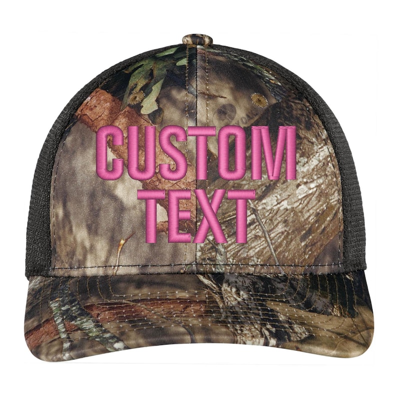 May include: A black and brown camouflage trucker hat with a pink embroidered "CUSTOM TEXT" on the front.