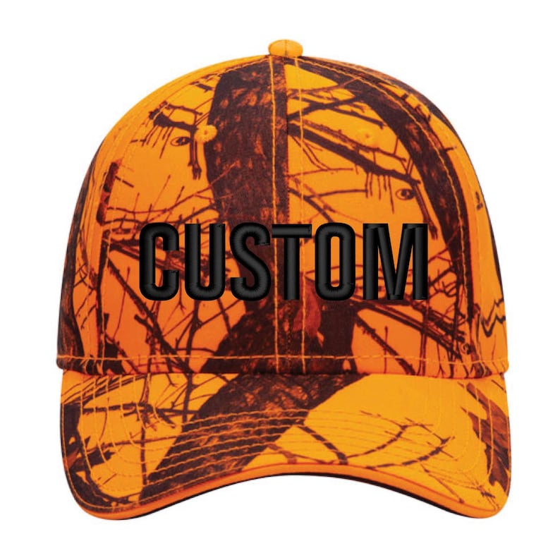 May include: An orange and brown camouflage baseball cap with the word "CUSTOM" embroidered in black. The cap has a curved brim and a structured crown, suitable for outdoor activities.