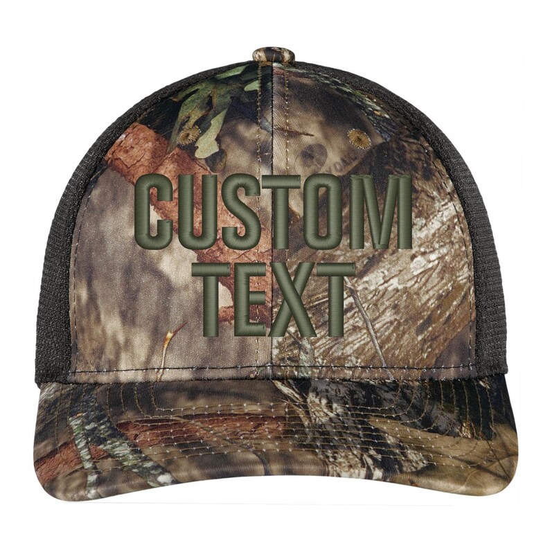 May include: A black and camouflage trucker hat with a black mesh back. The front of the hat has the words "CUSTOM TEXT" embroidered in green.