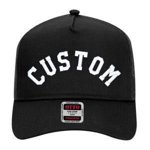 May include: Black trucker hat with the white word "CUSTOM" across the front. The hat has a mesh back and a curved brim. The hat also has a small tag that says "OTTO" and "TRUCKER".