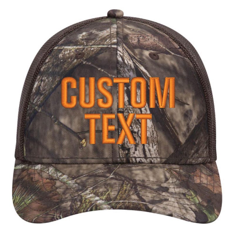 Op de afbeelding: Een bruine en oranje camouflage trucker cap met een zwart mesh achterpaneel. De pet heeft de tekst "CUSTOM TEXT" in oranje geborduurd op de voorkant.