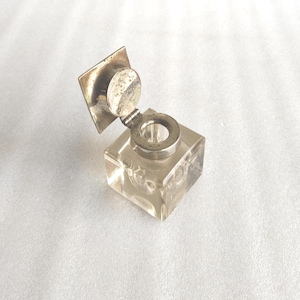 Op de afbeelding: Een vierkante inktpot van helder glas met een scharnierend metalen deksel en een vierkante achterplaat. De metalen onderdelen hebben een doffe, zilverkleurige afwerking. De inktpot heeft een ronde opening aan de bovenzijde.