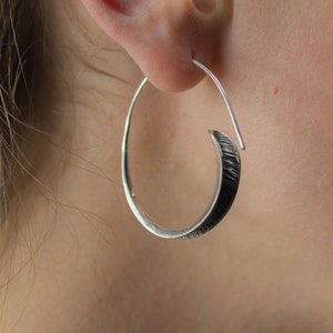 May include: Silver hoop earrings with a twisted design. The earrings are silver with a textured finish.