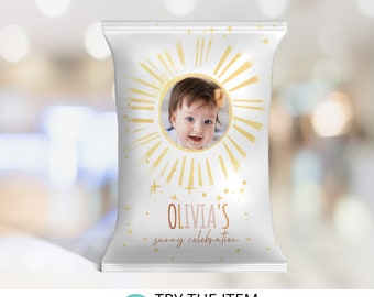 May include: A white chip bag with a gold sunburst design and a photo of a baby girl. The text "Olivia's sunny celebration" is printed in pink and gold.