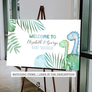 May include: Welcome to Elizabeth & George Baby Shower sign with a blue and green dinosaur illustration and tropical leaves.