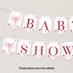 May include: A white banner with red letters spelling "BABY SHOW" with pink and red hearts scattered throughout. The banner has a pink bow on each end.