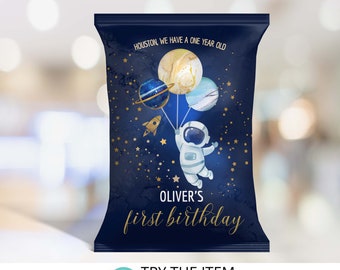 May include: A blue and gold astronaut-themed party favor bag with the text "HOUSTON, WE HAVE A ONE YEAR OLD" and "OLIVER'S first birthday".