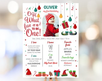 May include: A Christmas-themed first birthday milestone poster for a baby named Oliver. The poster features a photo of the baby, a red and green color scheme, and details about the baby's first year, including favorite foods, toys, and milestones. The poster includes the text "Oh What Fun It Is To Be One!"