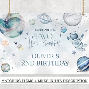 May include: A blue and white space-themed birthday sign with the text "Let's Blast Off... Two the Moon! Oliver's 2nd Birthday" and illustrations of planets, stars, a rocket, and an astronaut.