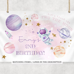 May include: A pink and white birthday banner with the text "let's blast off TWO THE MOON" and "Emmy's 2ND BIRTHDAY!"  The banner features an astronaut, planets, stars, and a rocket.