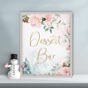 May include: A framed sign with the words "Dessert Bar" in gold script, surrounded by watercolor roses, pinecones, and greenery. A small snowman figurine with a black top hat and pink arms is in the foreground.