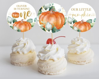 May include: Three round cupcake toppers with a fall theme. The toppers feature a watercolor pumpkin with green leaves and gold glitter accents. The text on the toppers reads "Oliver is turning one", "Our little pumpkin", and a single pumpkin with gold glitter accents.