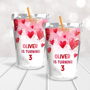 May include: Two pink and red juice pouches with gold glitter and hearts. The pouches have a label that says "Oliver is turning 3".