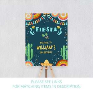 K&ouml;nnte beinhalten: Ein blaues und wei&szlig;es Willkommenszeichen f&uuml;r eine Fiesta-Motto-Geburtstagsparty. Das Schild sagt "Fiesta" und "Willkommen zu Williams 2. Geburtstag". Das Schild ist mit bunten Papierdekorationen, Kakteen und Maracas verziert.