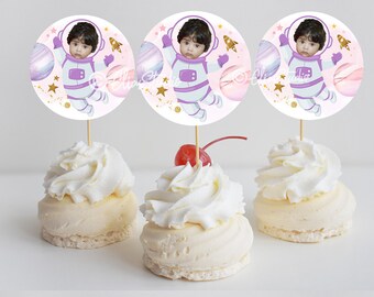May include: Three round cupcake toppers with a white background and a pink, purple, and gold space theme. Each topper features a photo of a baby in an astronaut costume, surrounded by stars, planets, and a rocket ship.