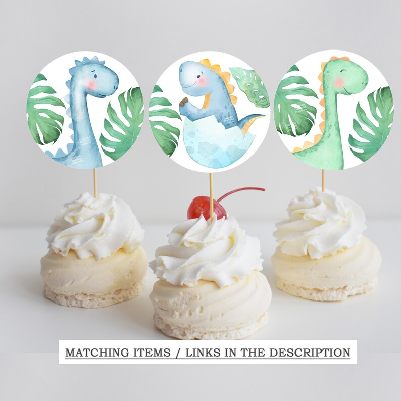 May include: Three round cupcake toppers featuring watercolor illustrations of dinosaurs with green and blue colors. The dinosaurs are surrounded by green leaves. The text "MATCHING ITEMS / LINKS IN THE DESCRIPTION" is at the bottom of the image.