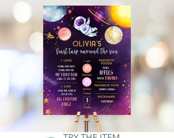 May include: A purple and gold space-themed first birthday milestone poster with a cute astronaut illustration. The poster lists the child's age, weight, height, favorite foods, toys, and nickname. The text reads "Olivia's first trip around the sun".