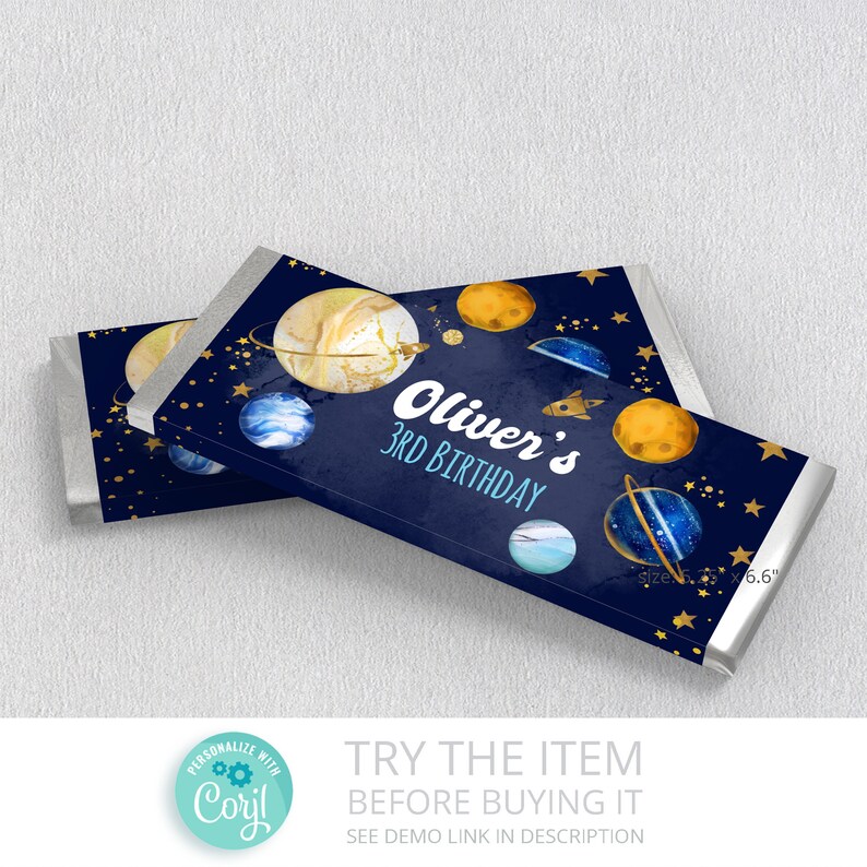 May include: A blue and gold chocolate bar wrapper with a space theme. It features planets, stars, and a rocket ship. The text on the wrapper says "Oliver's 3rd Birthday".