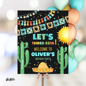 May include: A black welcome sign with colorful decorations, cacti, and a sombrero. The sign reads "Let's Three-Esta! Welcome to Oliver's Birthday Party!"