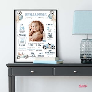 Op de afbeelding: Een ingelijste baby-mijlpaalafdruk met een foto van een baby. De afdruk bevat de naam van de baby, afmetingen (61 cm, 10 kg), favoriete dingen en andere details. Decoratieve ballonnen en raceautographics zijn inbegrepen.