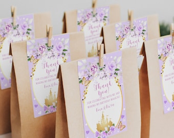 May include: Purple and gold thank you favor bags with a floral design and a castle illustration. The text on the bags reads "Thank you! For celebrating with me and making my birthday magical! Love Olivia."