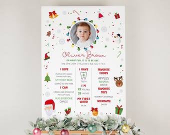 May include: A Christmas-themed first birthday milestone poster with a photo of a baby boy. The poster features a red, green, and white color scheme with festive decorations. It includes details about the baby's age, weight, height, favorite foods, toys, and first word. The text on the poster reads "Oliver Brown, Oh what fun, it is to be one, Sep 23rd, 2000x | 10:22 AM | BLb 12oz/19 in, I love, playing with daddy, playing with ball, my teddy bear, going to the park, I can, crawl and stand up, pick up toys, hug everyone, dance, I have, 4 teeth, I'm, 22 pounds, 29 inches, my first word, pa-pa, favorite foods, apples, banana, water, favorite toys, mommy's earrings, nickname, Santa".