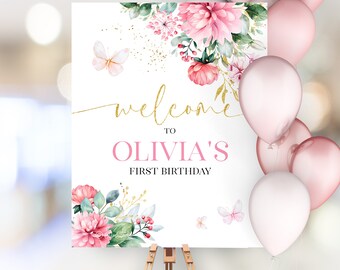 May include: Welcome to Olivia's First Birthday sign with pink and green floral design, gold glitter, and butterflies.