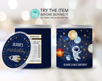 May include: A blue and gold can with a space-themed design featuring an astronaut holding balloons shaped like planets. The can has a sticker on the front that says "Oliver's first birthday".