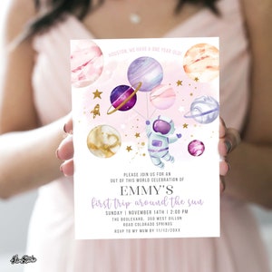 Puede incluir: Una invitación a una fiesta de cumpleaños de primer año con temática espacial rosa y morada con un astronauta de dibujos animados que sostiene globos con forma de planetas. El texto dice "Houston, tenemos un niño de un año!" y "Por favor, únase a nosotros para una celebración fuera de este mundo de la primera vuelta de Emmy alrededor del sol." La invitación incluye la fecha, la hora y el lugar de la fiesta, así como una fecha límite para confirmar asistencia.