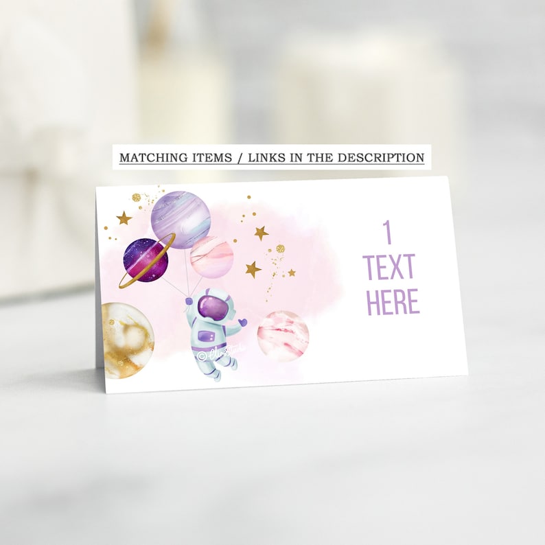 May include: A white card with a pink and purple watercolor background featuring an astronaut holding balloons shaped like planets. The text "1 TEXT HERE" is printed on the card.