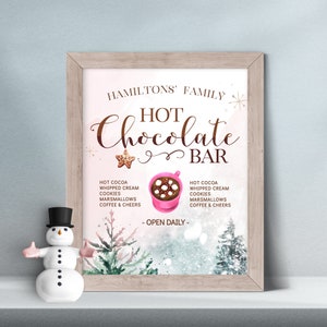 May include: A framed sign with the text "HAMILTONS' FAMILY HOT CHOCOLATE BAR" in brown script. The sign includes a list of hot chocolate ingredients and a pink mug graphic. A snowman figurine with a black top hat is in the foreground.
