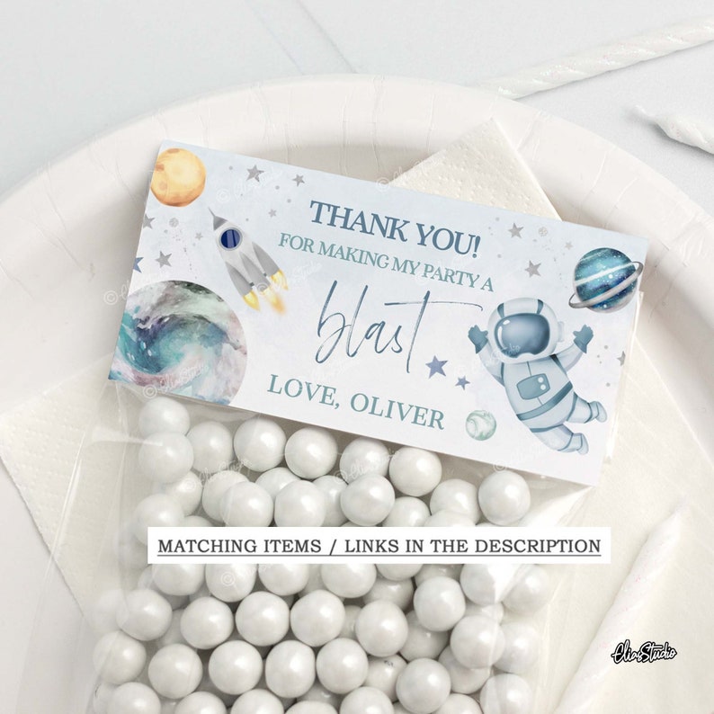 May include: A blue and white thank you favor bag with a space theme. The bag features an astronaut, planets, stars, and a rocket. The text on the bag reads "Thank you! For making my party a blast. Love, Oliver."