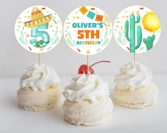 May include: Three cupcake toppers with a fiesta theme. The toppers feature a sombrero, a cactus, and a banner that says "Oliver's 5th Birthday".