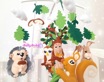 May include: A woodland-themed baby mobile with a brown tree trunk, green leaves, a gray hedgehog holding a mushroom, a brown owl perched on a branch, a brown squirrel holding a green sprig, and a brown rabbit.