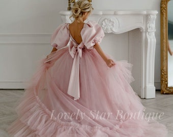 Puede incluir: Un vestido de tul rosa claro con una falda voluminosa y mangas abullonadas. La espalda presenta un gran lazo y una espalda baja. El texto "Lovely Star Boutique" es visible en la falda.