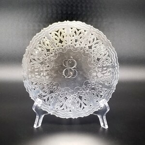 May include: A clear acrylic plate with a delicate lace design and the number "8" engraved in the center. The plate is on a clear acrylic stand.