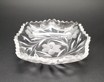May include: A clear glass square dish with a scalloped edge. The dish is etched with a floral design.