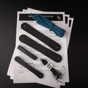 Op de afbeelding: Een doe-het-zelf sling-set met vier zwarte rechthoekige, leerachtige strips met voorgeponste gaten, een rol blauw en zwart gevlochten koord en een klein pakketje met het label needle and thread, op een wit instructieblad met de titel MAKE OWN SLING.