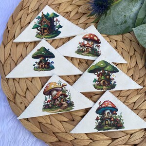 May include: Six triangular fabric bookmarks with whimsical mushroom house illustrations. Each bookmark features a different mushroom house with a unique design and color scheme. The houses are surrounded by greenery and flowers.