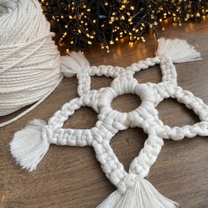 May include: A white macrame star with a circular design in the center. The star has tassels on each point.