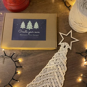 May include: A macrame Christmas tree hanger kit, including a cardboard box with the text "Create your own Macrame Tree Hanger". A finished macrame tree and wooden star are also visible. The kit includes everything needed to create a macrame tree hanger.