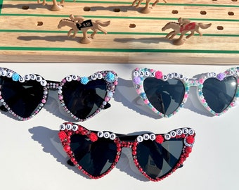 May include: Three pairs of heart-shaped sunglasses with black lenses and beaded embellishments. The sunglasses are decorated with colorful beads and letters spelling out "Talk Derby To Me" and "Run For The Roses".